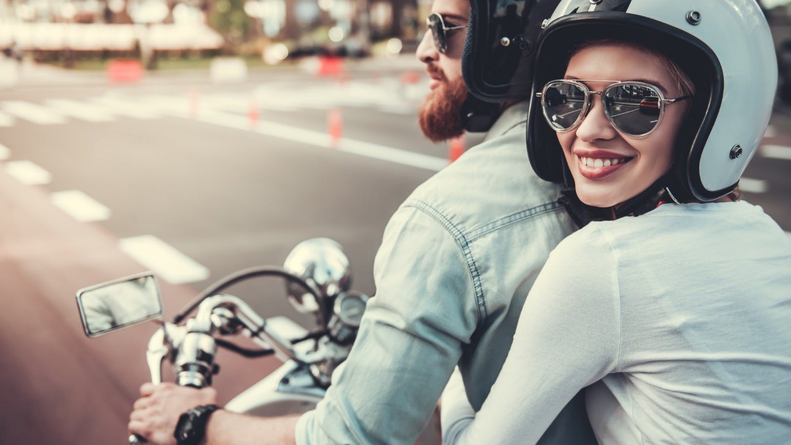 Een vrouw kijkt als bijrijder op een motor lachend naar ons om