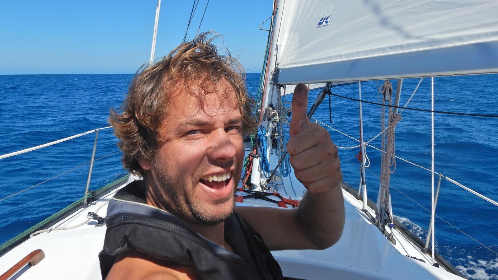 Werner staat op zijn zeilboot en steekt zijn duim naar ons op