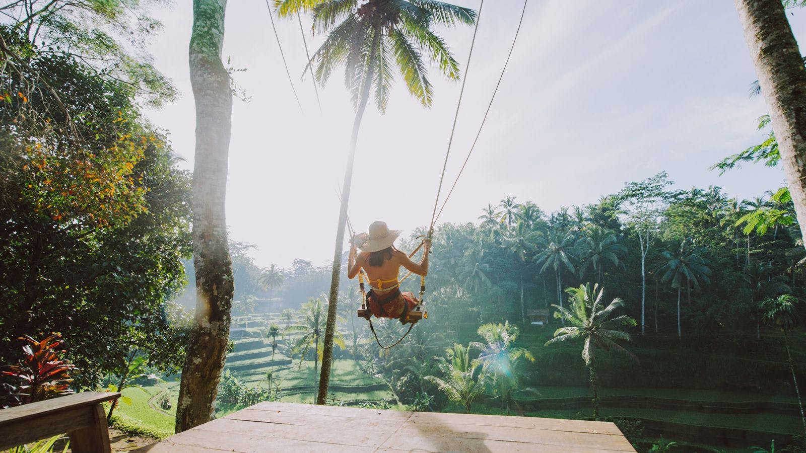 een vrouw zit op een hoge schommel met uitzicht op tropisch woud en rijstvelden