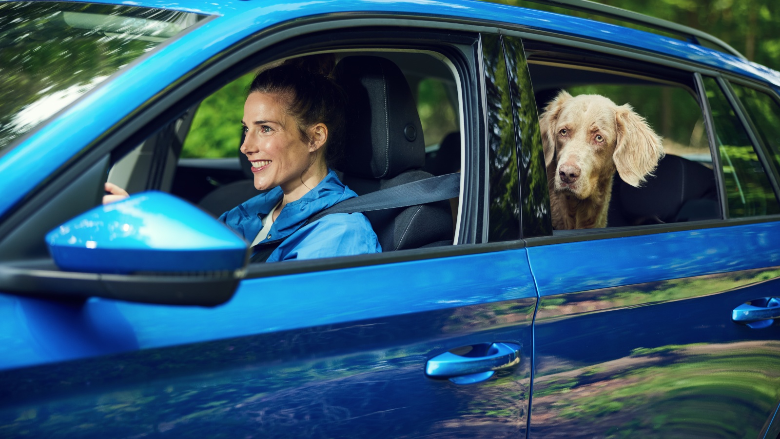 Vrouw zit lachend in de auto samen met hond