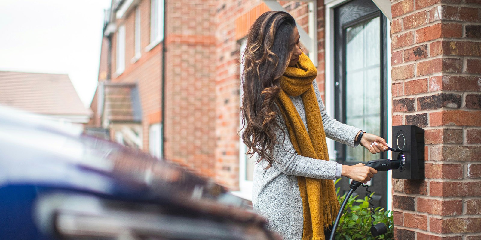 Vrouw komt thuis en koppelt de auto aan haar slimme laadpaal en bespaart zo kosten.