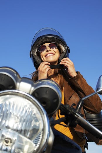 Lachende vrouw zit op haar motor met blauwe lucht