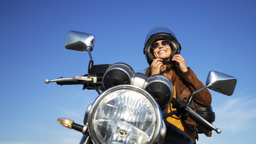 Lachende vrouw zit op haar motor met blauwe lucht
