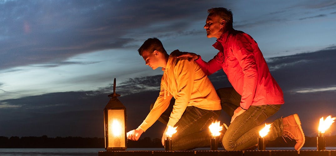 2 mannen laten bij een steiger brandende kaarsen in het water