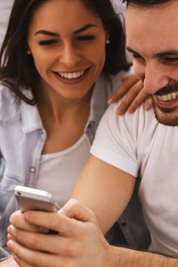 Een man en vrouw kijken lachend naar het scherm van een mobiele telefoon