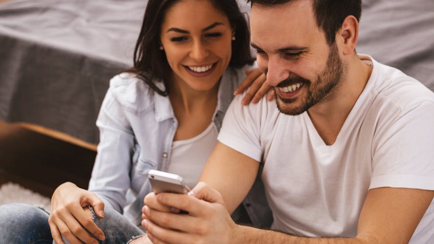 Een man en vrouw kijken lachend naar het scherm van een mobiele telefoon