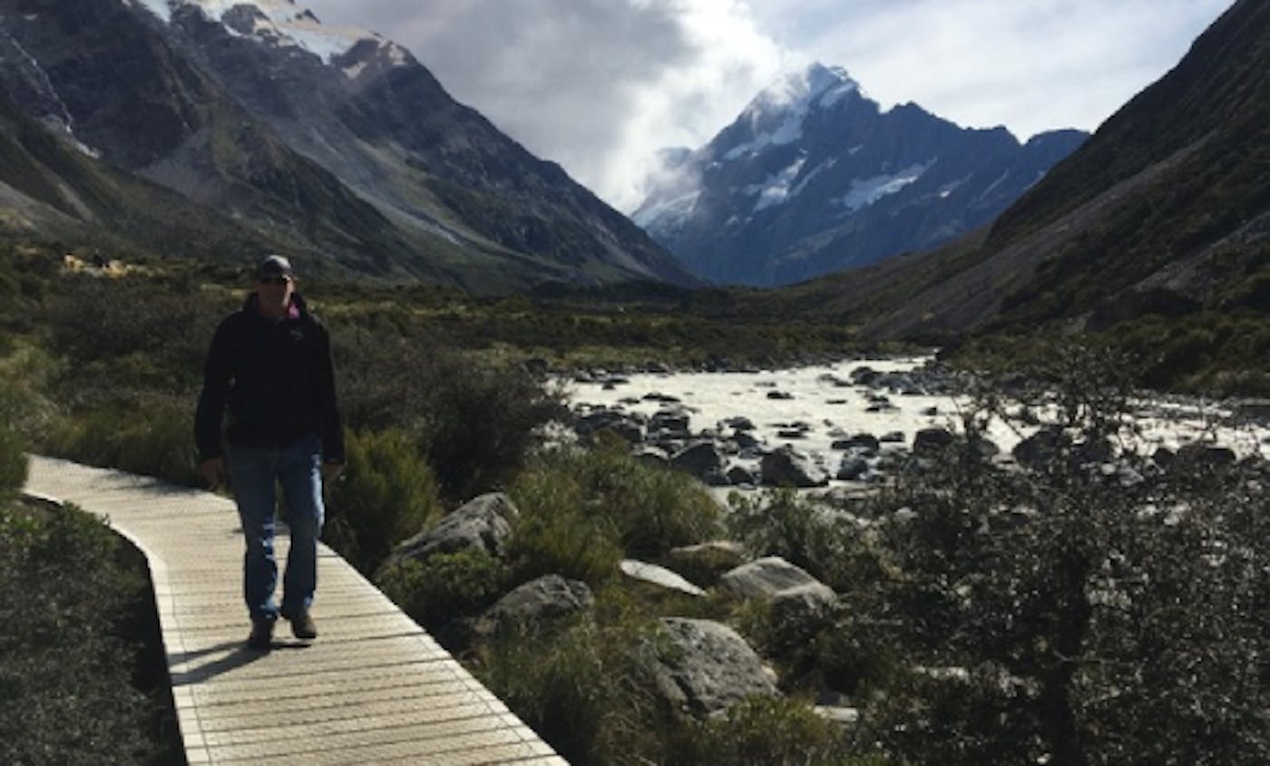 een man loopt op een goed onderhouden pad dat dwars door het ongerepte landschap van Nieuw-Zeeland loopt