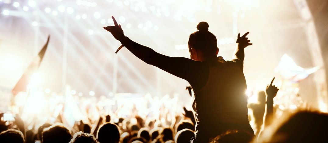 Persoon met knotje en witte hemd geniet op iemands schouders tijdens een concert op een festival