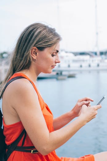 een vrouw is, zittend in een haventje, bezig op haar mobiele telefoon