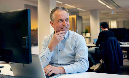 Man in blauwe blouse vertelt achter zijn bureau enthousiast over dat een reisverzekering meer verzekert dan alleen je spullen tijdens je studie in het buitenland