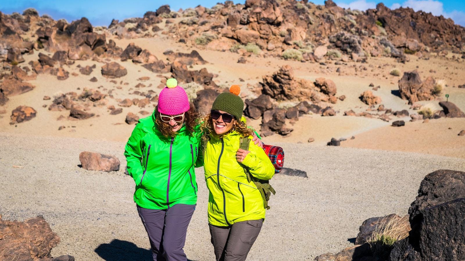 2 vrouwen in felgekleurde jassen lopen door een rotsachtige omgeving