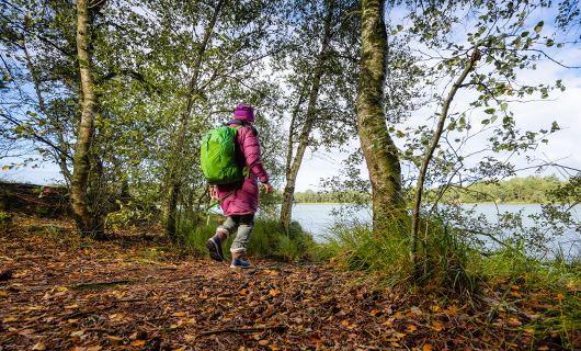 Susan loopt met grote groene rugzak richting bomen en een meertje