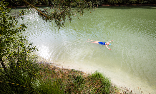 Susan drijft op haar rug in een door bos omzoomd meertje