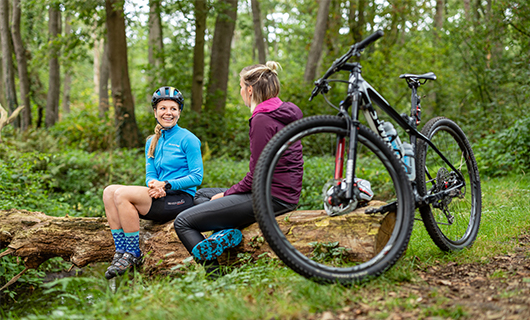 2 mensen zitten in gesprek op een boomstam, met een fiets op de voorgrond