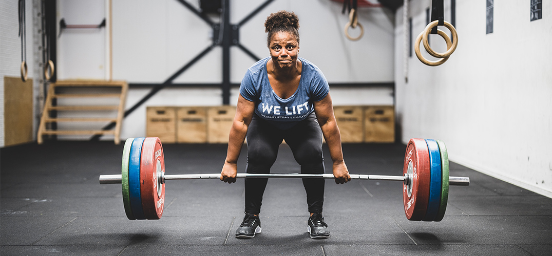 Miloushka tilt met ingespannen frons een halter op met aan elke kant 3 grote gewichten