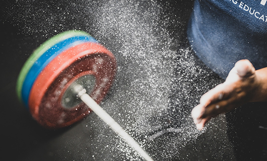 Een hand en rond dwarrelend magnesiumpoeder, met op de achtergrond een halter