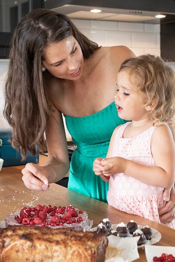 Sanne helpt haar dochtertje bij het versieren van een taart vol fruit