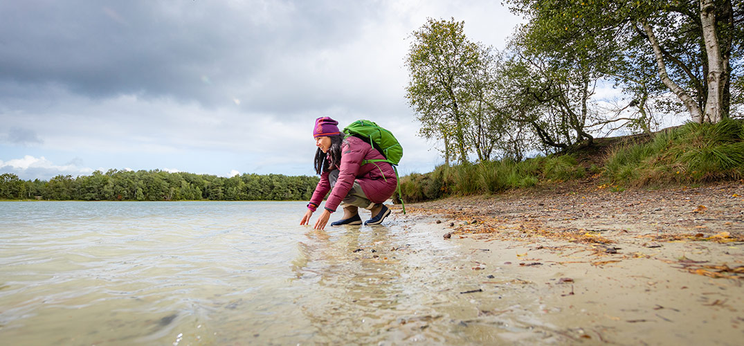Susan zit gehurkt aan de waterkant met haar handen in het water