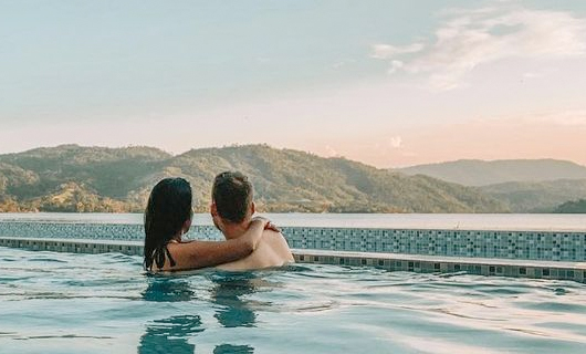 Andrea heeft haar armen om Lars heen terwijl ze vanuit een zwembad over het mooie landschap uitkijken