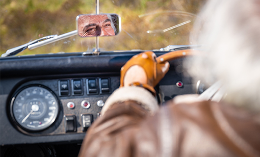 Claude kijkt genietend in zijn achteruitkijkspiegel