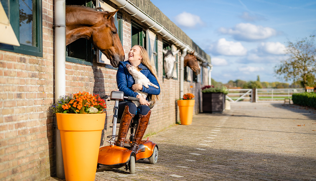 Esra houdt lachend haar hondje in haar armen terwijl haar paard haar aanhaalt