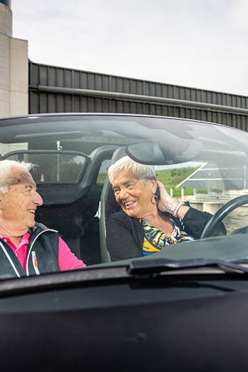 Jan en Miep kijken genietend naar elkaar in hun zwarte Porsche Boxster
