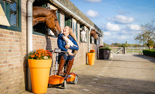 Esra houdt lachend haar hondje in haar armen terwijl haar paard haar aanhaalt