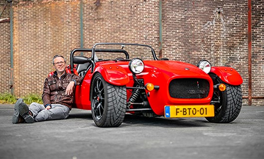 Martijn zit op de grond tegen zijn rode sportauto aan