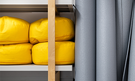 grijze opgerolde yogamatten tegen een kast met gele zitkussens