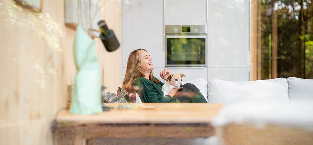 Tanja zit op de bank met haar hondje op schoot in haar boshuis