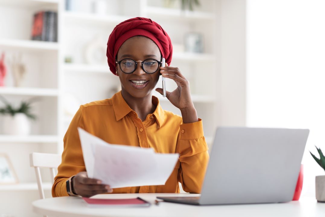 Een jonge vrouw voert een belangrijk telefoongesprek. Met haar laptop en papieren bij de hand regelt ze doelgericht haar zaken.