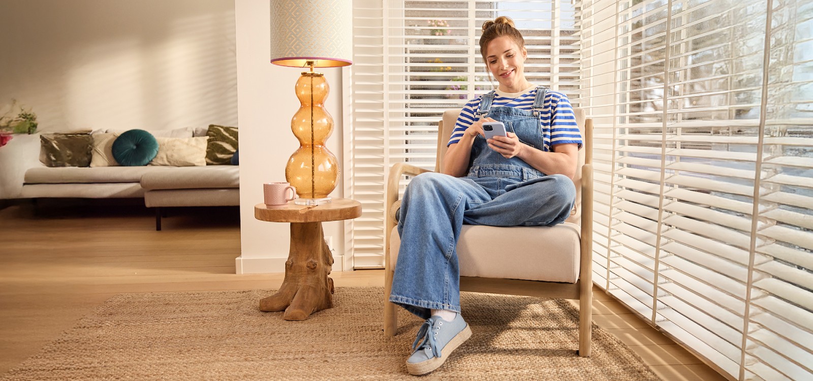 Vrouw regelt thuis op haar telefoon de automatische verlichting, 1 van de onderdelen van slimme inbraakpreventie. 