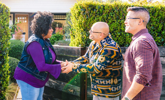 3 mensen staan voor een tuin en schudden elkaar de hand.