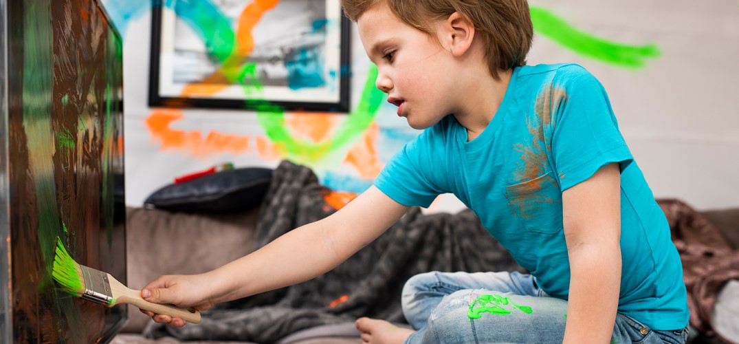 Een klein kind met kwast in de hand. De muren en tv-scherm hebben gekleurde verf vegen.