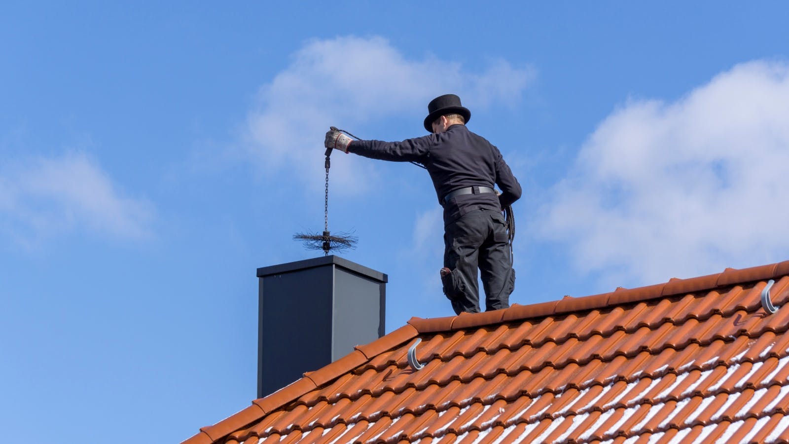 Een schoorsteenveger staat op het dak en laat een ragebol zakken in de schoorsteen