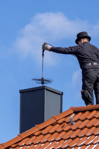 Een schoorsteenveger staat op het dak en laat een ragebol zakken in de schoorsteen