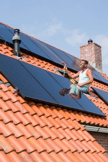 Een meneer installeert zonnepanelen op het dak