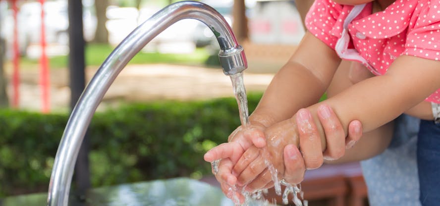 Grote handen helpen kleine handjes wassen onder een lopende kraan