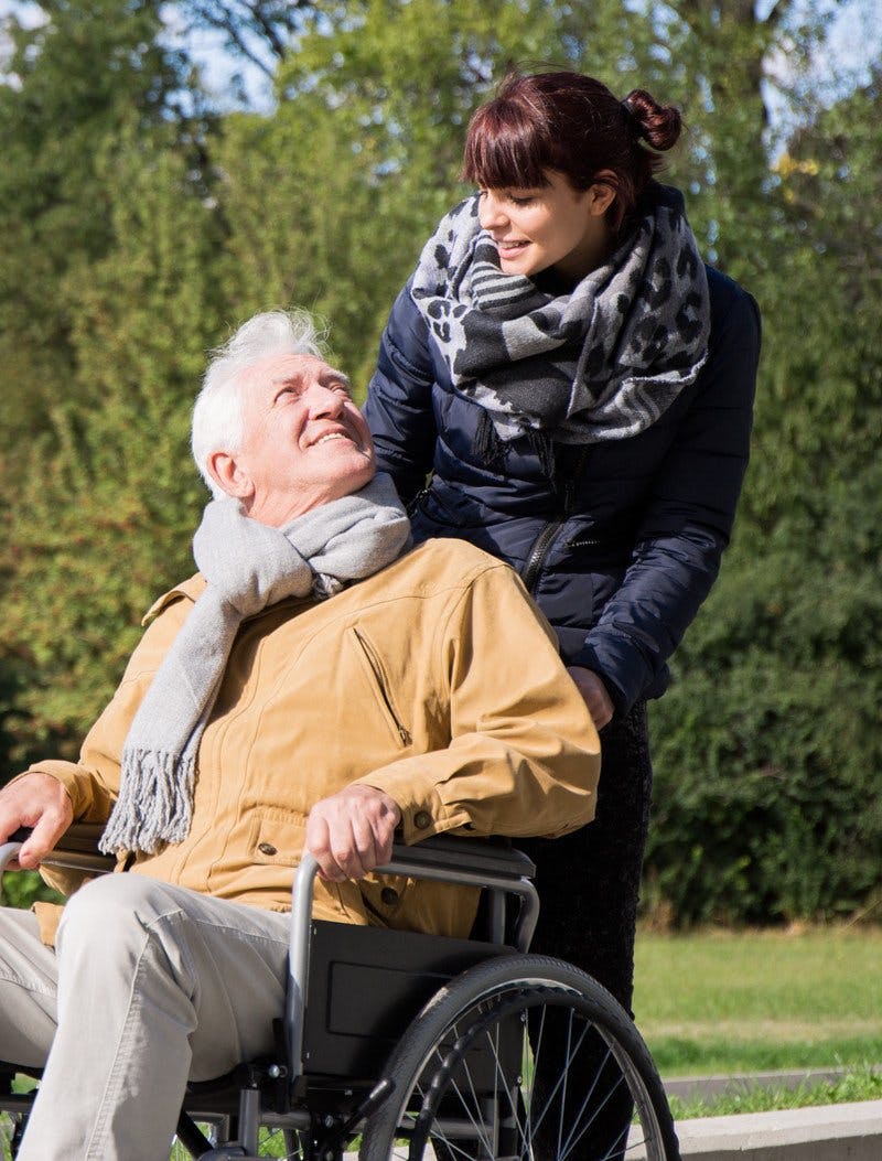 Een vrouw duwt een oudere heer in een rolstoel, ze kijken elkaar lachend aan