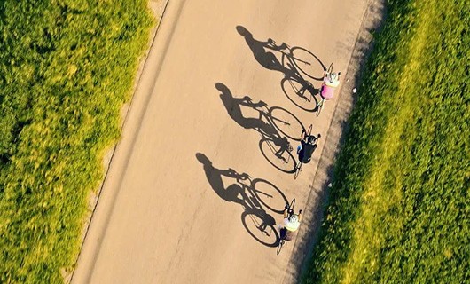 3 fietsers op de weg, van boven gezien en met lange schaduwen