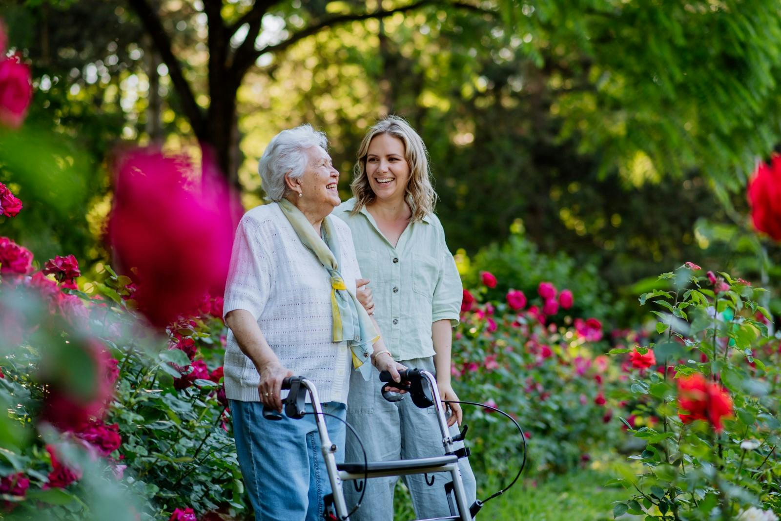 Oude vrouw loopt en lacht in de tuin met mantelzorger