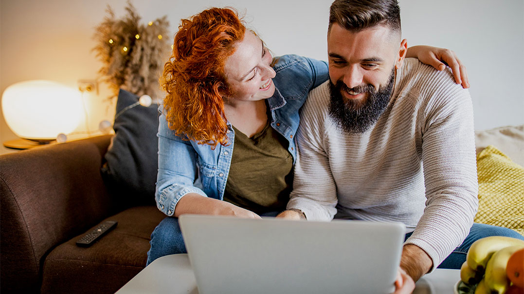 Een stel zit knus op de bank. Samen verdiepen ze zich in een online reanimatiecursus op de laptop.