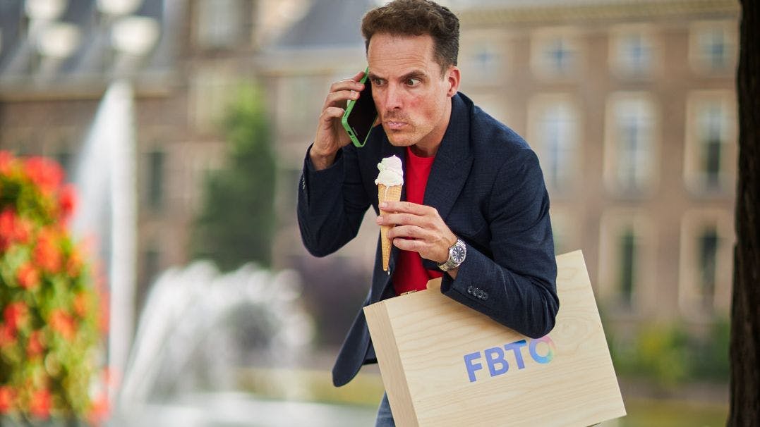 Man met ijsje in hand loopt met koffer met FBTO erop