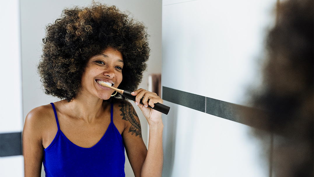 Een vrouw met een stralende glimlach poetst haar tanden met een houten e-brush van Smyle. Ze is klaar om de dag fris en vol energie te beginnen. 