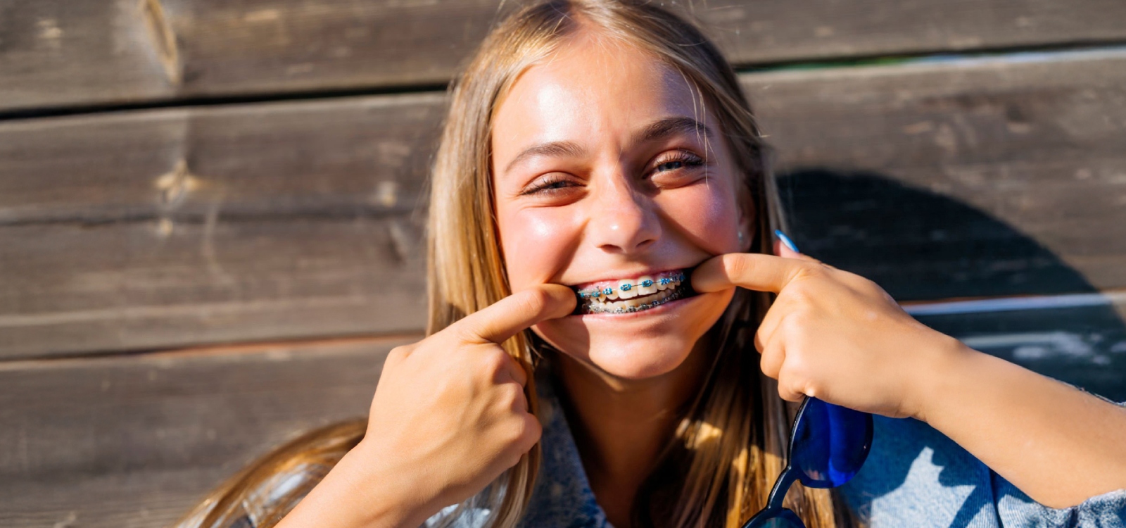 meisje van 12 met blond haar laat trots haar beugel zien die ze vanaf haar leeftijd goed kan gebruiken. 