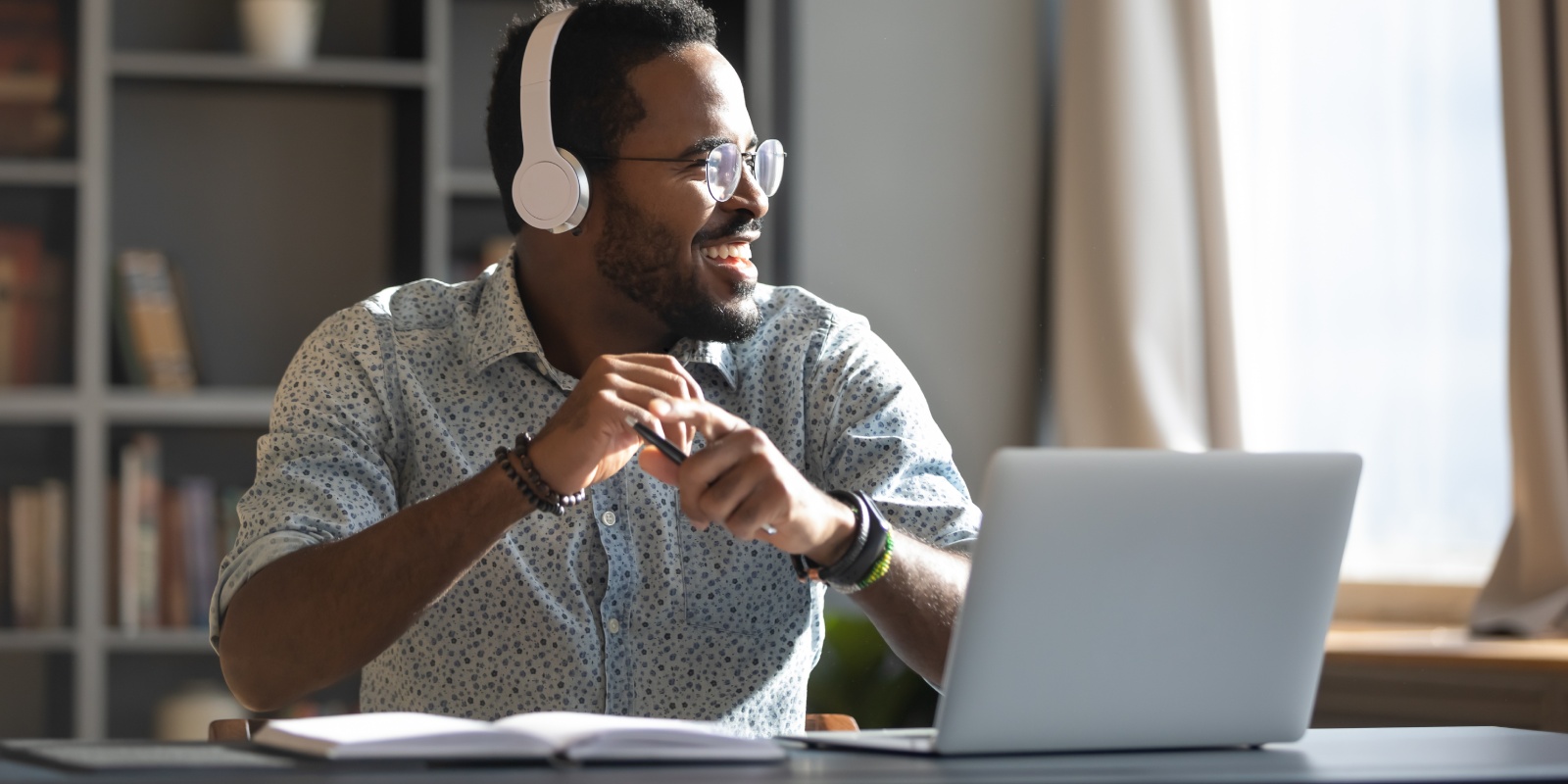 Lachende man met witte koptelefoon zoekt achter zijn laptop uit welke zorgkosten aftrekbaar zijn.