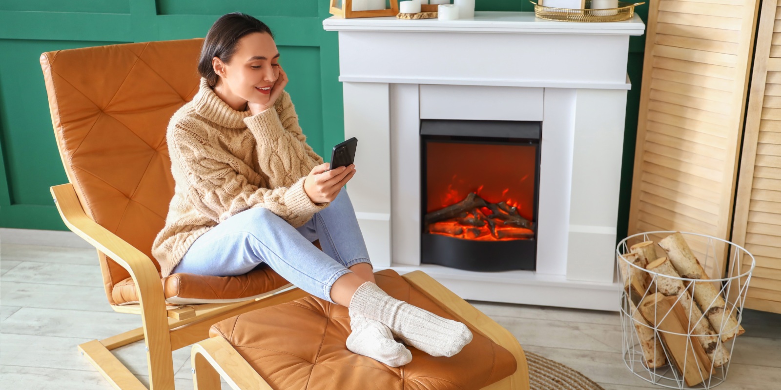 Vrouw rond 30 jaar met donkerbruin haar zit ontspannen naast haar open haard in januari haar zorgverzekering te wijzigen op haar smartphone